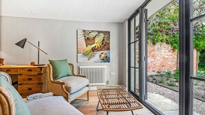 Una sala de estar moderna con un ventanal grande, un escritorio de madera, una silla de mimbre y un cuadro en la pared.