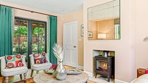Una sala de estar acogedora con chimenea, una mesa redonda de madera, dos sillones y un espejo grande en la pared.