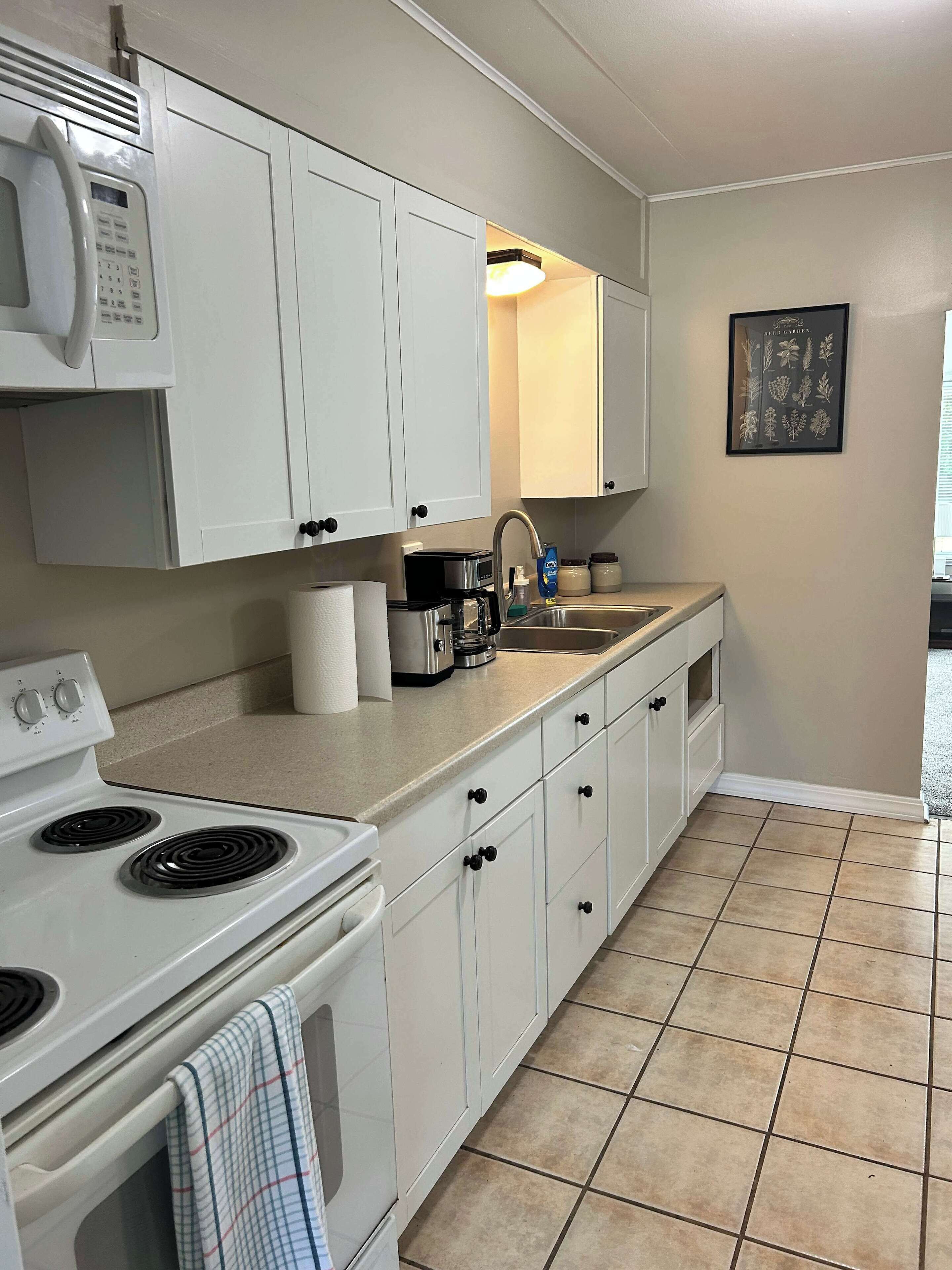 A kitchen with white cabinets, a stove, a microwave, a coffee maker, and a sink.