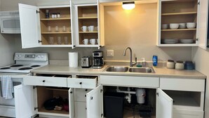A compact kitchen with white cabinets, a stove, a sink, and a coffee maker. - Loveland Family Home: 3BR, 2 Living Areas, Free Parking (Loveland)