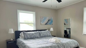 A neatly made bed with a floral-patterned bedspread, two bedside lamps, and a large window with blinds. - Loveland Family Home: 3BR, 2 Living Areas, Free Parking (Loveland)