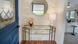 A room with a glass console table, a mirror, a vase with flowers, and a lamp.