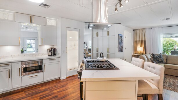 A modern kitchen with white cabinetry, a central island, and a dining area with a beige sofa.