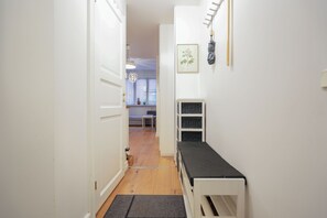 Un couloir étroit avec un banc blanc, une porte et un porte-objets fixé au mur.