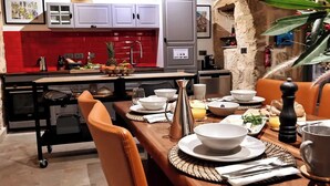 Cozinha moderna com armários cinza, painel de fundo vermelho e área de refeições com mesa de madeira posta para uma refeição.
