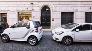 Two white cars parked on a cobblestone street in front of a building with a black door and a sign that reads "VINCHIC". - Fabulous Cozy Pantheon Apartment (Roma)