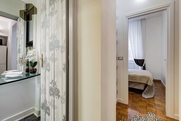 A hotel room with a glass partition, a bed with a white bedspread, and a wooden floor.