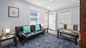 A modern living room with a black leather sofa, teal cushions, a coffee table, and a framed picture on the wall. - Two Bedroom Oceanside Condo Steps from the Beach (Ocean City)