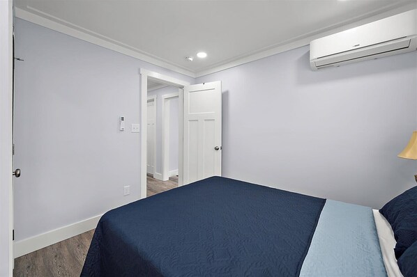 A bedroom with a bed, an air conditioning unit, a door, and a hallway. - Two Bedroom Oceanside Condo Steps from the Beach (Ocean City)