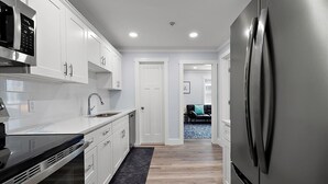 A modern kitchen with white cabinetry, stainless steel appliances, and a black rug. - Two Bedroom Oceanside Condo Steps from the Beach (Ocean City)