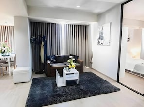 A modern living room with a sofa, a coffee table with a vase, and a view of a bedroom through a glass door. - Arun Haus 39 (Bangkok)