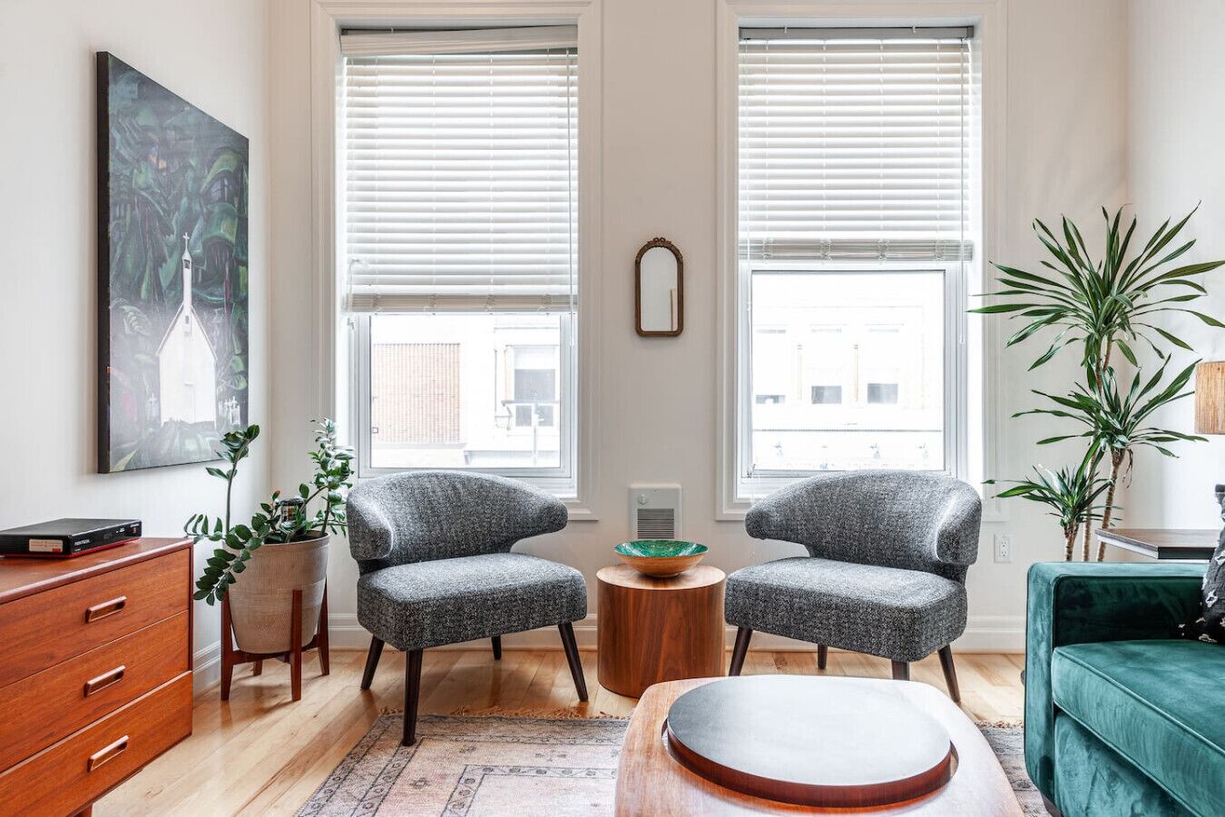 A modern living room with two grey armchairs, a wooden coffee table, a green sofa, a wooden cabinet, and a painting on the wall.