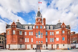A large, historic red brick building with a central clock tower, multiple windows, and a flagpole with a Canadian flag.