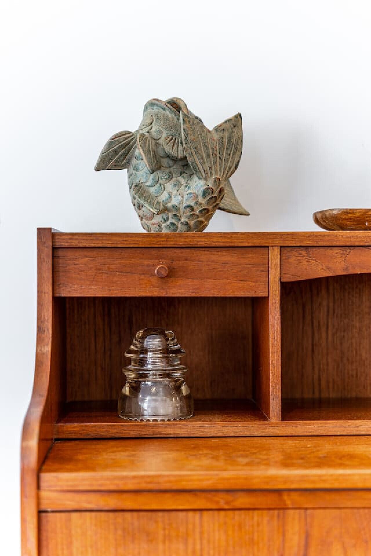 A wooden cabinet with a decorative fish sculpture on top and a glass jar in the lower compartment.