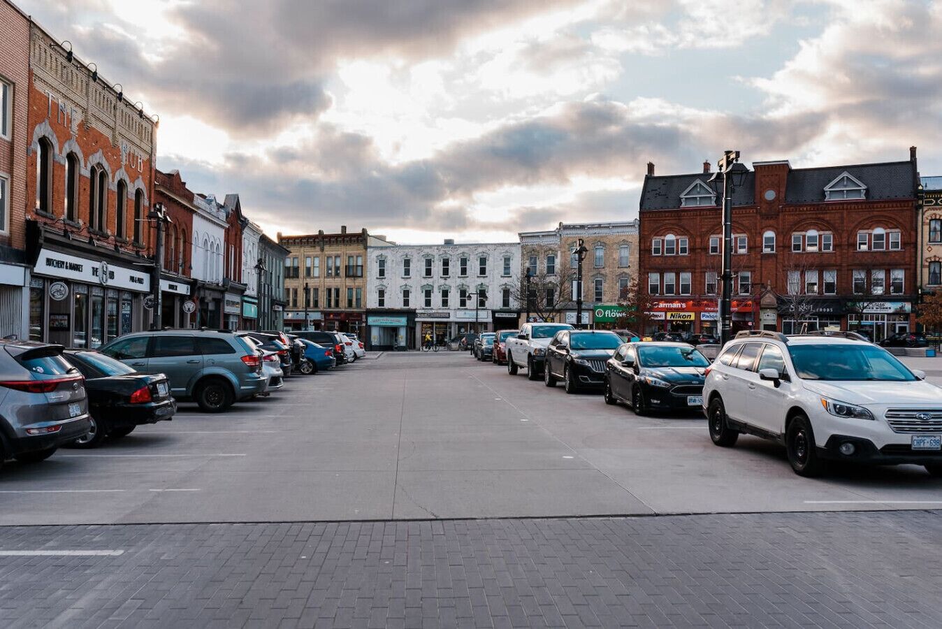 Une rue bordée de voitures garées et de bâtiments aux devantures de magasins variées.