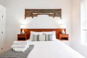 A neatly made bed with white linens, two bedside tables with lamps, and a decorative wooden piece above the bed.