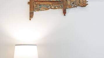 Un lit bien fait, avec un oreiller blanc et un plaid rayé, une table de chevet en bois avec une lampe bleue, et un élément décoratif en bois accroché au mur au-dessus du lit.