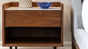 Une table de chevet en bois, sur laquelle se trouvent une lampe et un bol bleu.