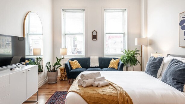 Une chambre moderne avec un lit, une télévision, un canapé et deux fenêtres.
