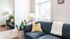 Un salon moderne avec un canapé bleu foncé, un plaid blanc et une plante en pot.