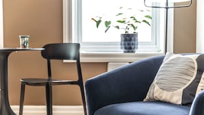 A living room with a dark blue sofa, a black chair, a small table, and a potted plant by the window.