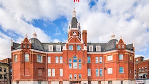 A large, historic red brick building with a prominent clock tower and a Canadian flag.