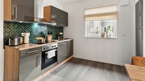 A modern kitchen with stainless steel appliances, wooden cabinets, and a green tiled backsplash.