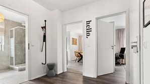 A modern interior with a wooden floor, white walls, and a visible bathroom with a shower.