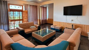 A modern living room with beige sofas, a glass coffee table, and a flat-screen TV mounted on the wall. - Noni’s Dream Villa (Kullu)