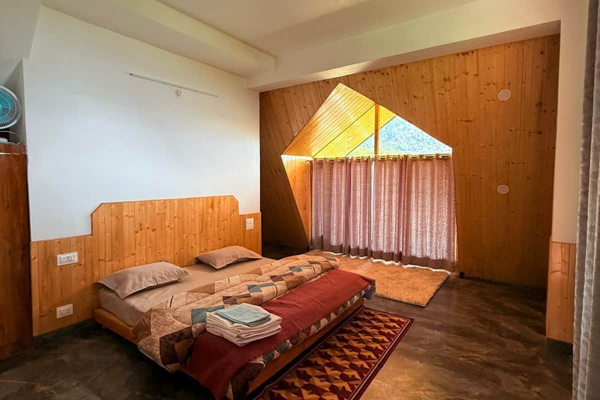 A bedroom with a wooden headboard, a bed with a patterned bedspread, a small rug, and a window with curtains.