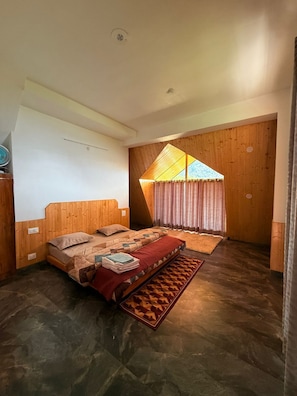 A bedroom with a wooden headboard, a bed with a patterned bedspread, a small rug, and a window with curtains. - Noni’s Dream Villa (Kullu)