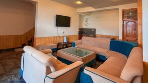 A modern living room with a sectional sofa, a coffee table, and a flat-screen TV mounted on the wall. - Noni’s Dream Villa (Kullu)