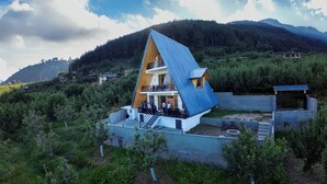 A modern house with a sloped roof, a balcony, and a small garden area. - Noni’s Dream Villa (Kullu)