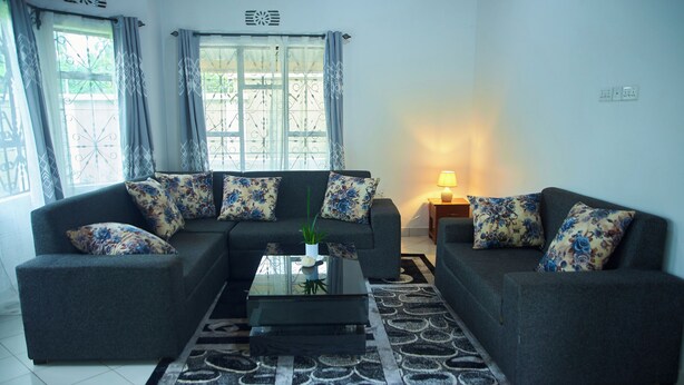 A living room with a grey sofa set, a glass coffee table, and a patterned rug. - A Little Paradise in Arusha – Serenity with Stunning Mountain Views (Arusha)