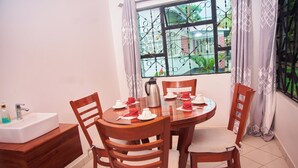 A dining area with a round table, four wooden chairs, a white sink, and a window with decorative iron bars. - A Little Paradise in Arusha – Serenity with Stunning Mountain Views (Arusha)
