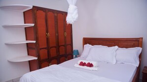 A neatly made bed with white linens, a wooden wardrobe with multiple doors, and a blue bedside lamp. - A Little Paradise in Arusha – Serenity with Stunning Mountain Views (Arusha)