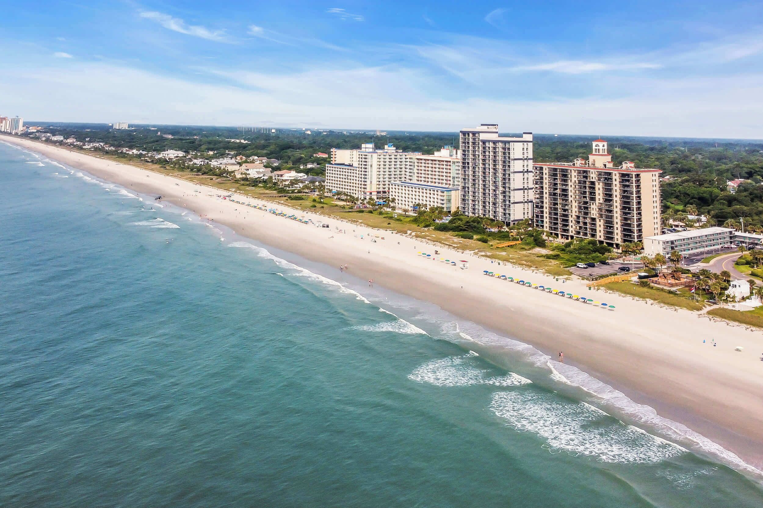 Een kusthotel met meerdere hoge gebouwen, een strand en een heldere lucht.