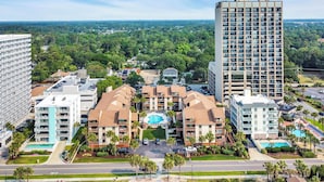 A hotel complex with multiple buildings, a central pool area, and surrounding greenery. - Anchorage by the Sea Ocean View Balconies and Pool (Myrtle Beach)