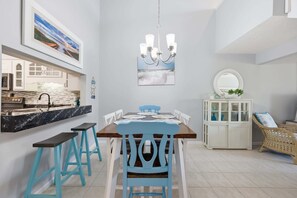 A dining area with a wooden table, blue chairs, a chandelier, a white cabinet, and a wicker chair. - Anchorage by the Sea Ocean View Balconies and Pool (Myrtle Beach)
