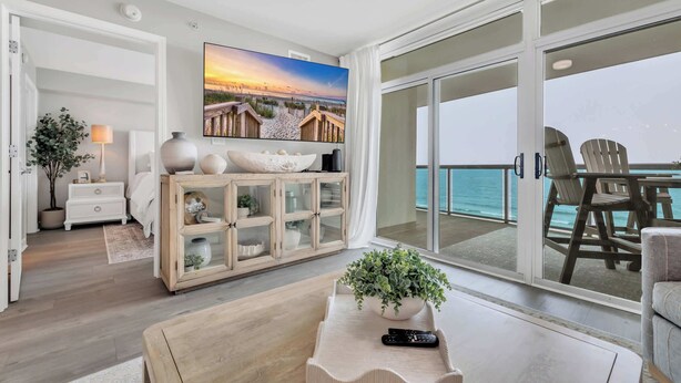 Amplia sala de estar con televisor grande, mueble de madera y vista al océano.