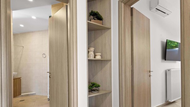 Une salle de bain moderne avec une douche, des toilettes et un lavabo. On y trouve des portes en bois et un mur blanc sur lequel est fixé un téléviseur.