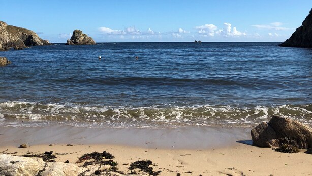 A beach with clear blue water, rocky outcrops, and a sandy shore.