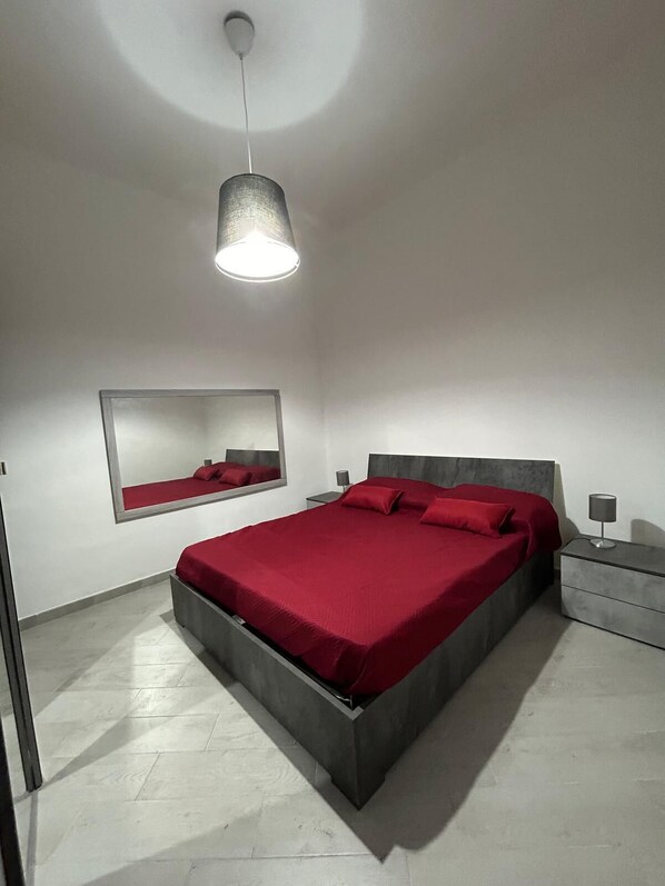 Une chambre à coucher moderne avec un grand lit, une table de chevet, une commode, un luminaire suspendu et un miroir au mur.