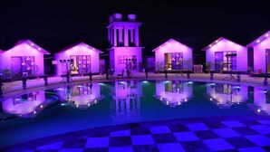 Un área de piscina con varios edificios pequeños, cada uno de estilo arquitectónico diferente, rodeada por un estanque reflectante.