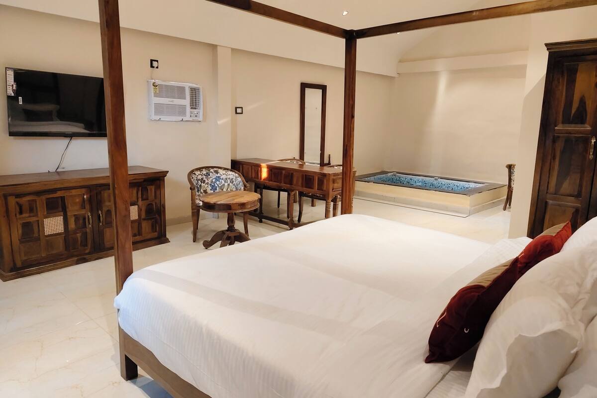 Un dormitorio con cama de dos plazas, un escritorio de madera, una silla, un televisor y una bañera.