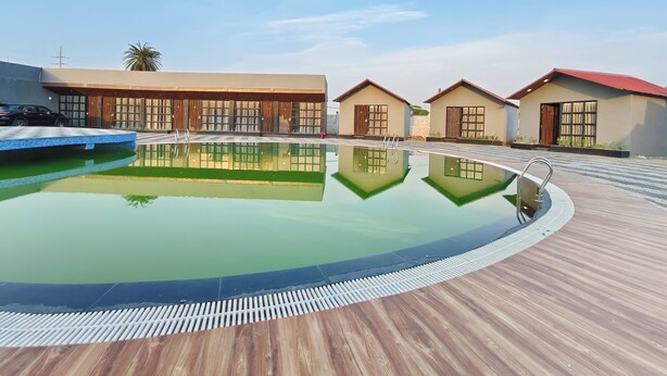 Una piscina con plataforma de madera, rodeada de edificios modernos con ventanas amplias y techo rojo.