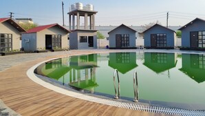 Una piscina con cubierta de madera, rodeada de edificios pequeños de diseño moderno.