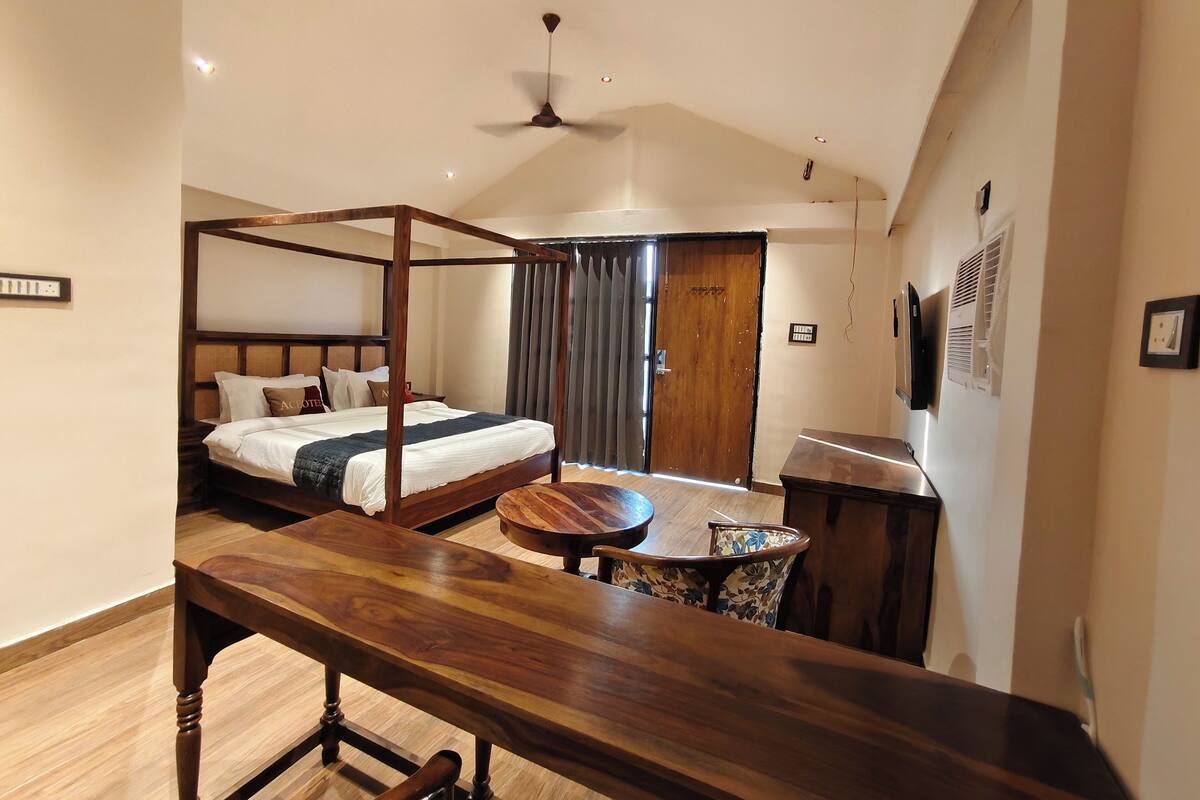 Habitación de hotel con cama con dosel, un banco de madera, una mesita pequeña y un ventilador de techo.
