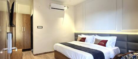 A modern hotel room with a wooden bed, a ceiling fan, an air conditioning unit, and a television.
