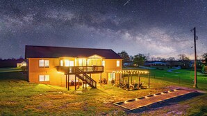 Ein zweistöckiges Haus mit überdachter Terrasse, umzäunter Garten und sternenklarer Nacht.